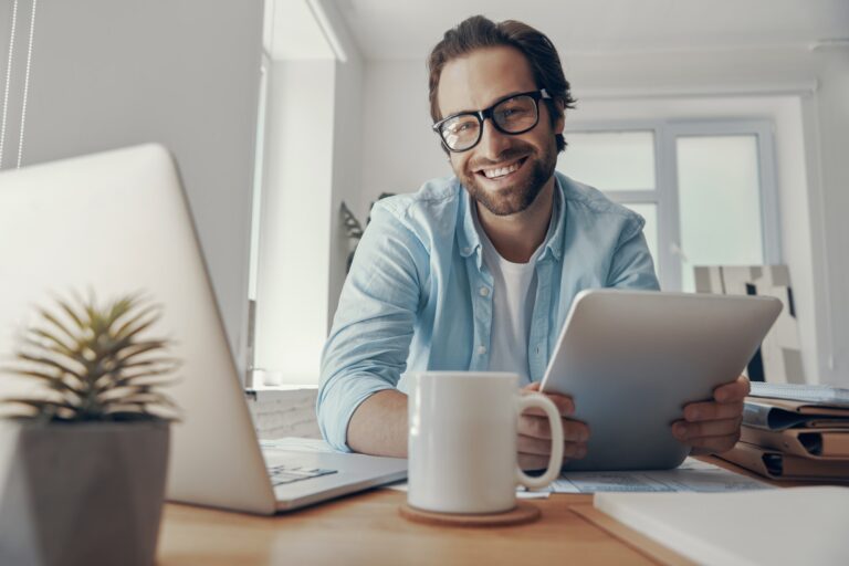 Happy young man using technologies while sitting at his working place in office